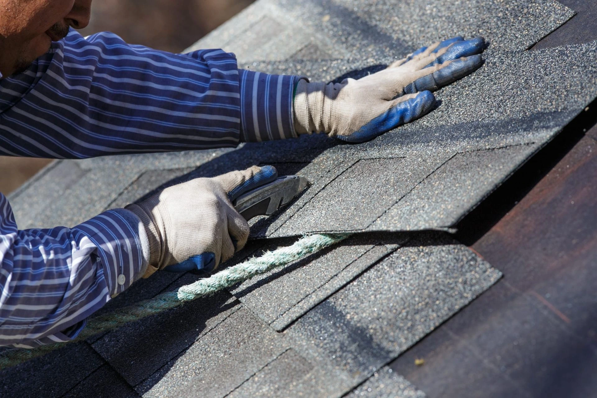 Roofing professional lifting and inspecting asphalt shingles to assess shingle condition, underlayment exposure, and potential roof damage.