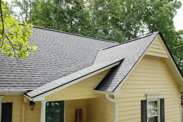 Close-up view of an aging gray asphalt shingle roof on a single-family home with gutters and wood siding