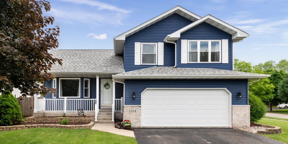 A well-maintained two-story home with clean asphalt shingle roofing and blue vinyl siding on a sunny day.